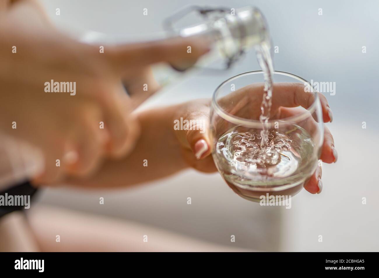 Verser de l'eau. Gros plan versant de l'eau fraîche purifiée de la bouteille sur une table sur un fond flou naturel Banque D'Images