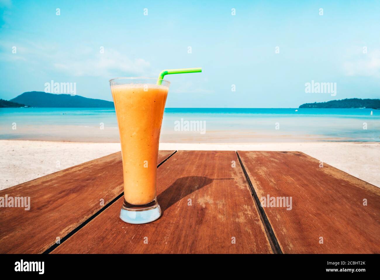 Un verre de jus d'orange se trouve sur une table en bois. Cocktail sur le fond de la mer bleue. Vacances, vacances, été, plaisir concept. Fruit Banque D'Images