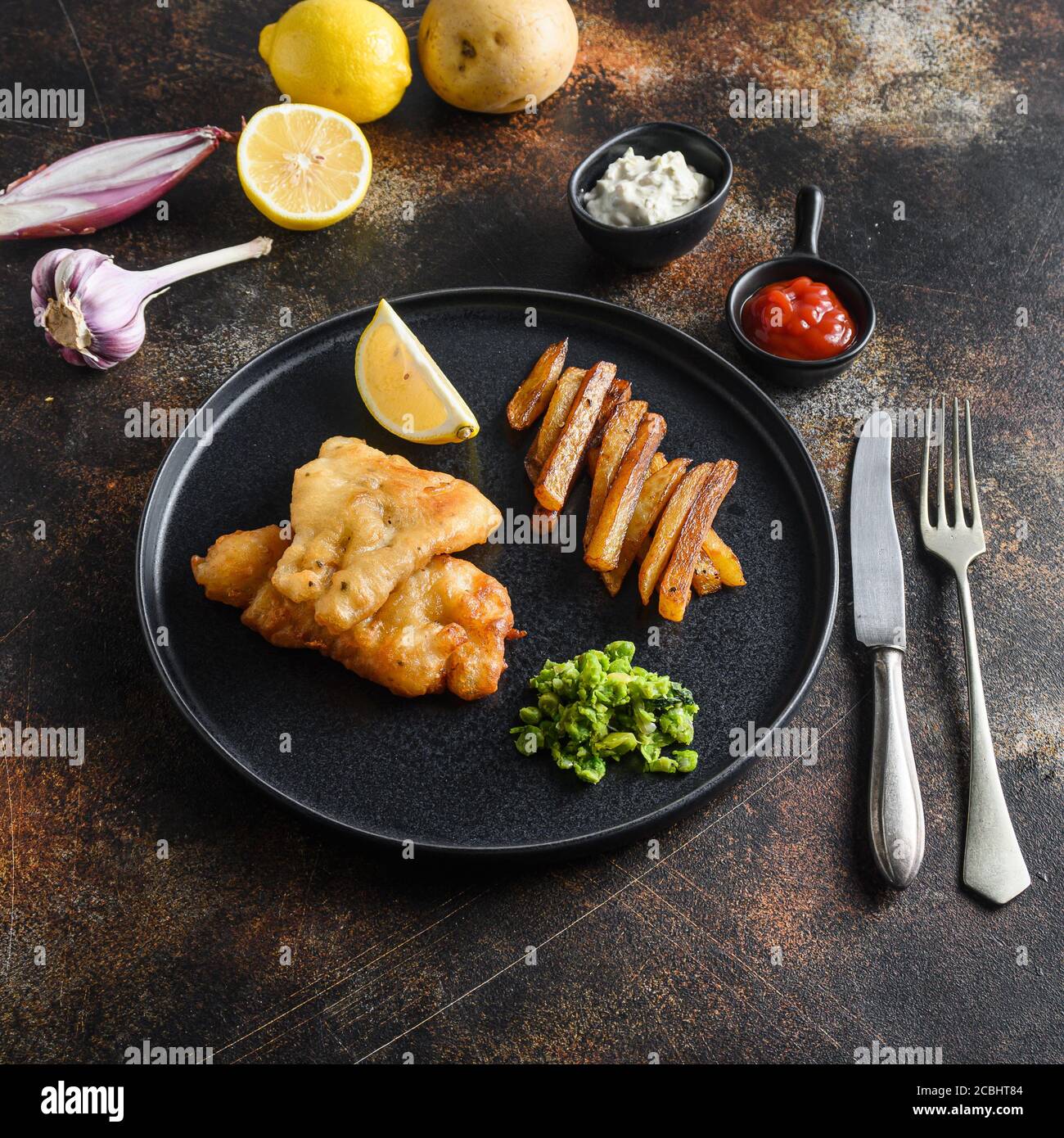fish and chips avec de la morue et des frites cuites à la bière et un côté de la sauce tartare et des petits pois sur l'assiette noire sur le haut de fond de style rustique ancien en métal Banque D'Images