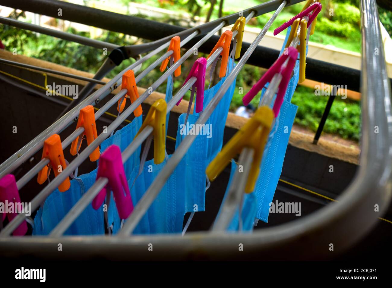 Un bouquet de masques bleus sont pendus sur une tige en tissu pour le séchage après les avoir nettoyés pour réutilisation. Masques réutilisables avec clips pendus Banque D'Images