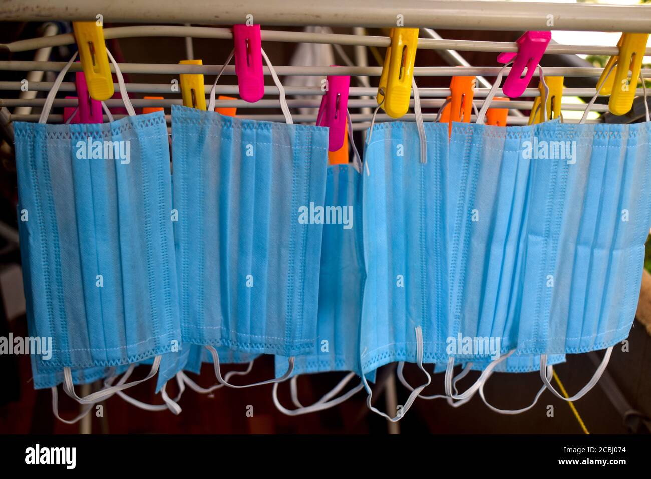 Un bouquet de masques bleus sont pendus sur une tige en tissu pour le séchage après les avoir nettoyés pour réutilisation. Masques réutilisables avec clips pendus Banque D'Images