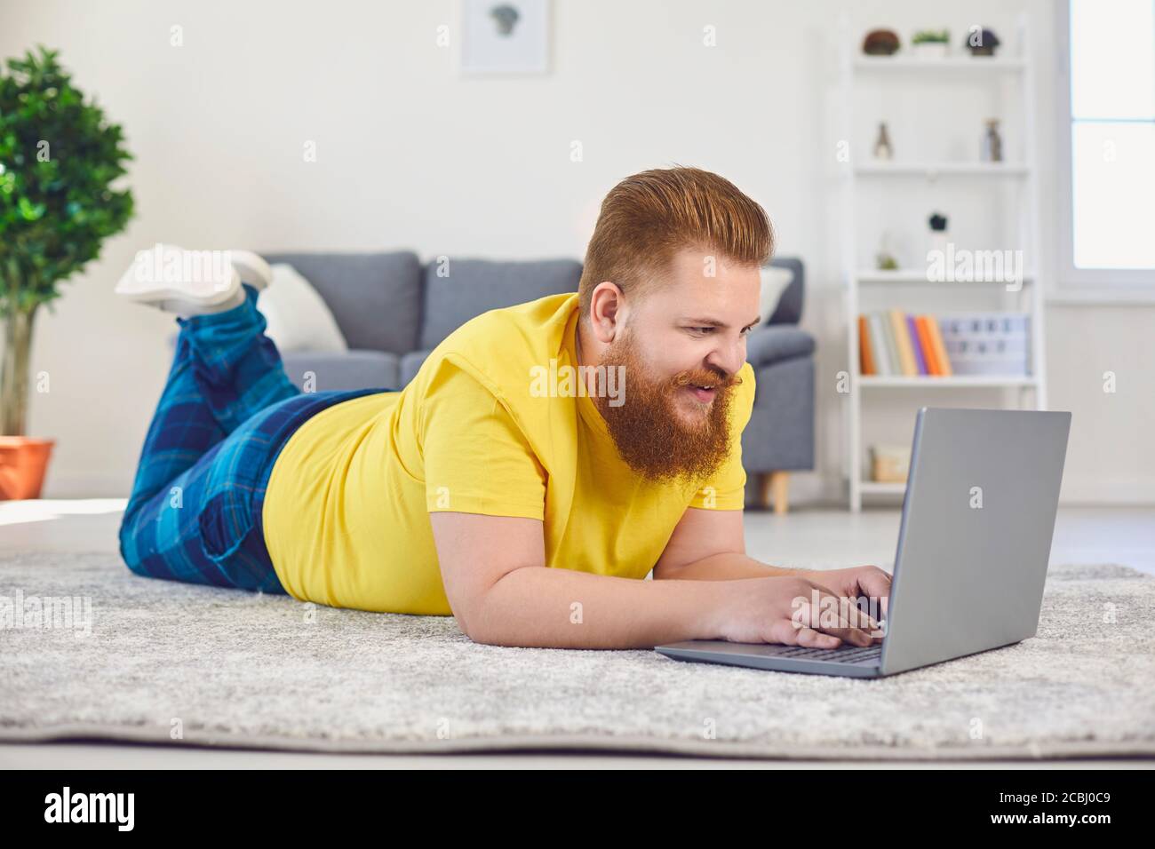 Date de communication de la formation en ligne. Un homme drôle avec une barbe tape dans un ordinateur portable tout en étant allongé sur le sol à la maison Banque D'Images