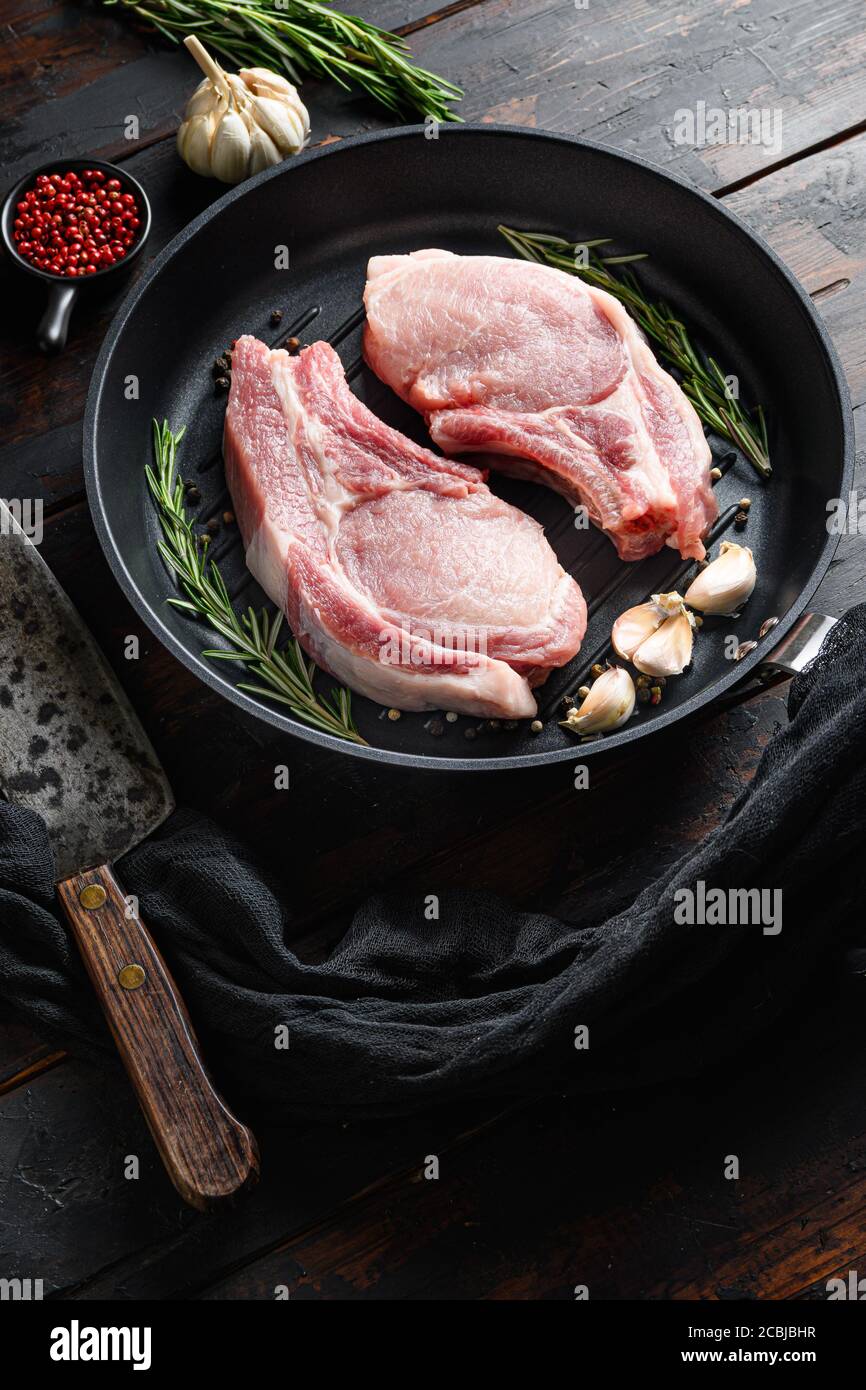 Rôti de porc cru dans une poêle sur un table de cuisine rustique en bois  avec des ingrédients de poivre de romarin à l'ail côté du couteau de la  grille et du
