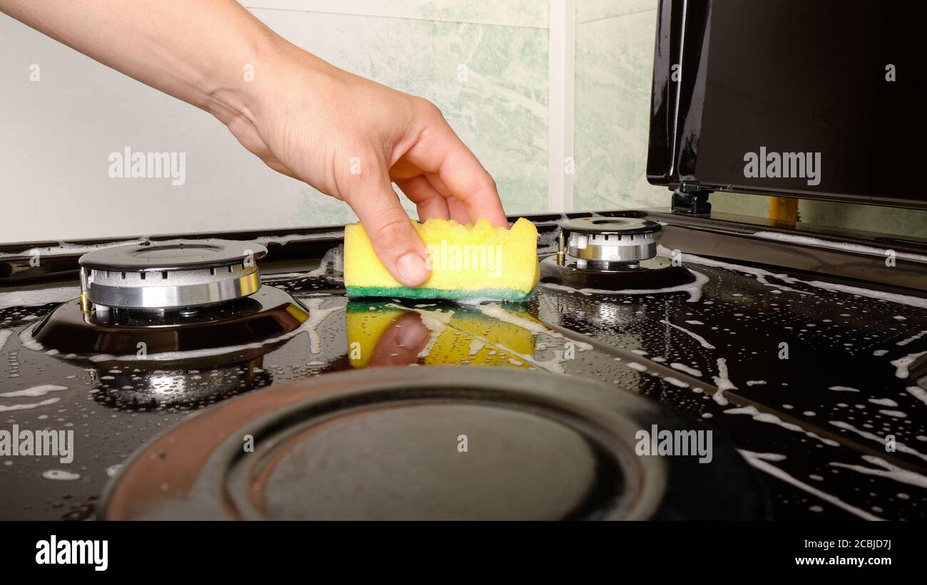 nettoyage de surface, femme lave cuisinière à gaz avec un linge de toilette jaune et un détergent. Banque D'Images