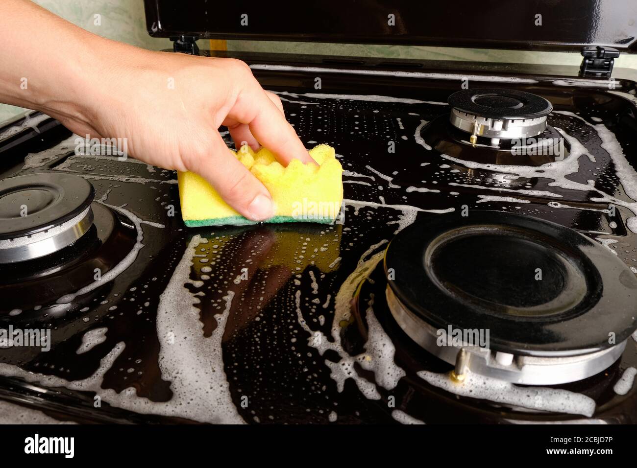 femme nettoie la cuisinière à gaz avec un débarbouillette et de la mousse, le nettoyage de surface, le nettoyage de la cuisine, les appareils de cuisine. Banque D'Images