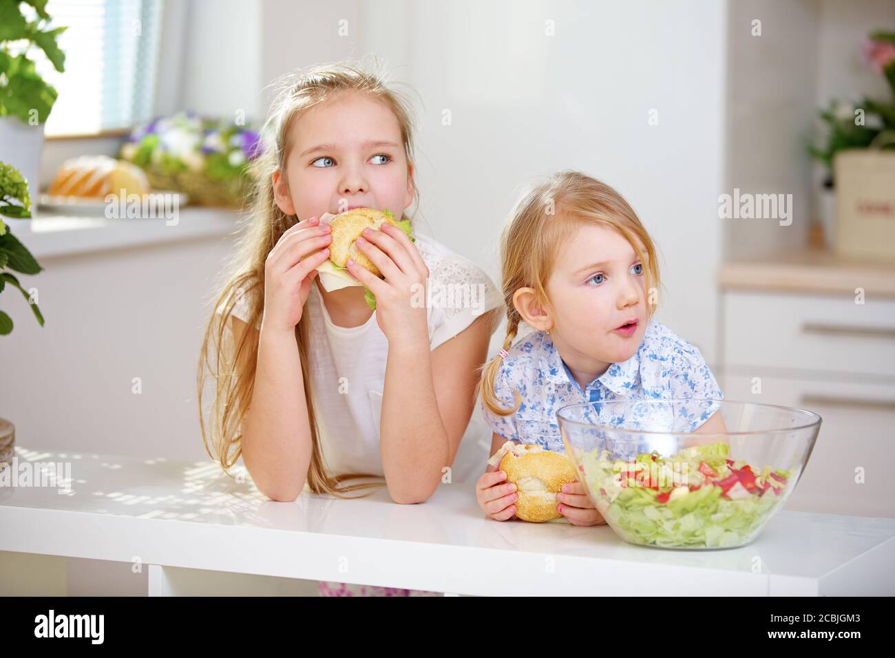 Deux enfants mangent des petits pains avec des saucisses et du fromage dans le cuisine Banque D'Images