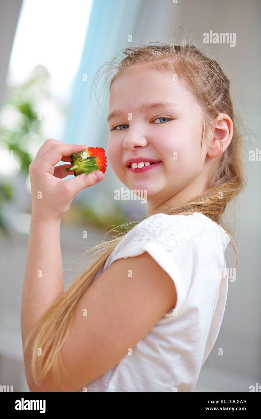 Une fille qui rit mange une fraise fraîche en été Banque D'Images