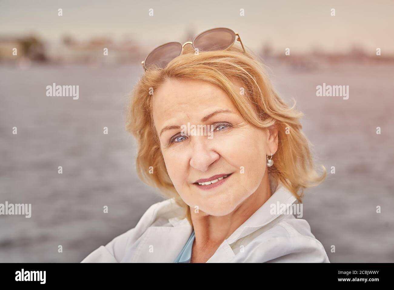 Portrait d'une femme blanche de race blanche d'âge attrayante et charmante, âgée d'environ 62 ans, avec des cheveux blonds et des lunettes de soleil. La dame retraité a un repos dans la cour Banque D'Images