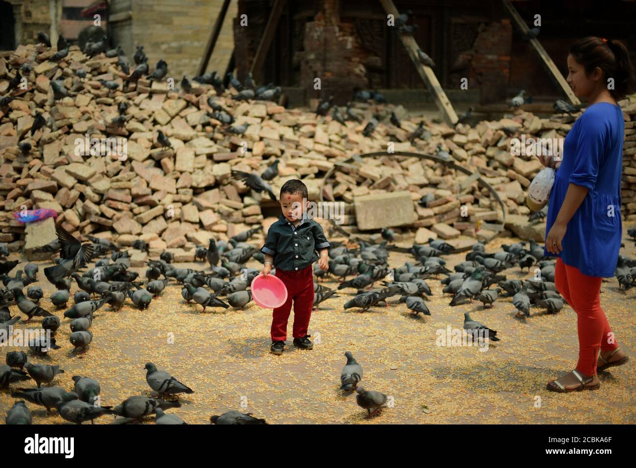 Un enfant ayant du temps de loisirs entre une pile de briques et un troupeau de colombes à Katmandou Durbar Square, Katmandou, Népal. Banque D'Images