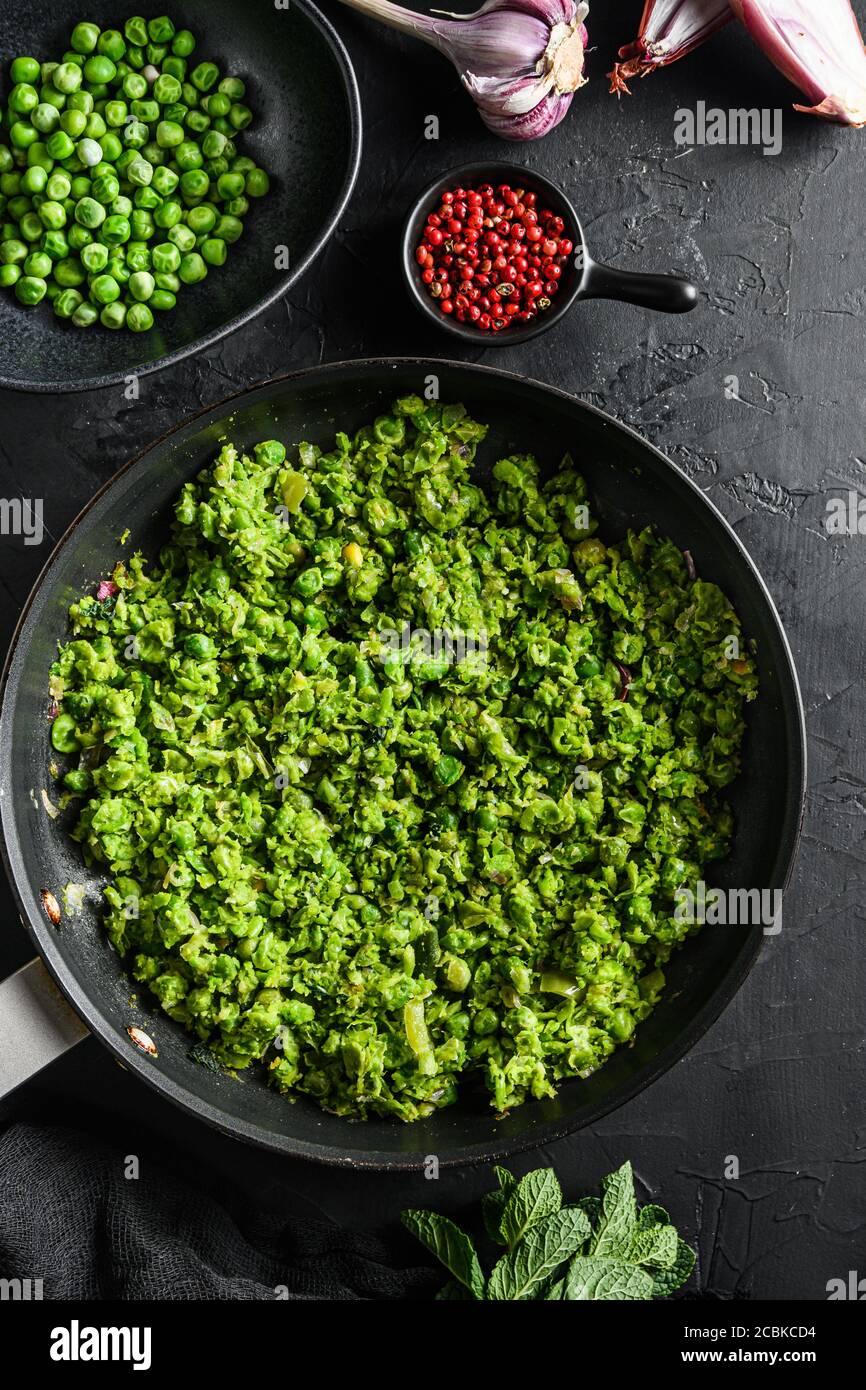 Les petits pois sont cuits dans une poêle et les petits pois dans un bol avec du poivre d'échalote à la menthe et du sel sur la surface en pierre noire vue de dessus de la nourriture bio keto gros plan Banque D'Images