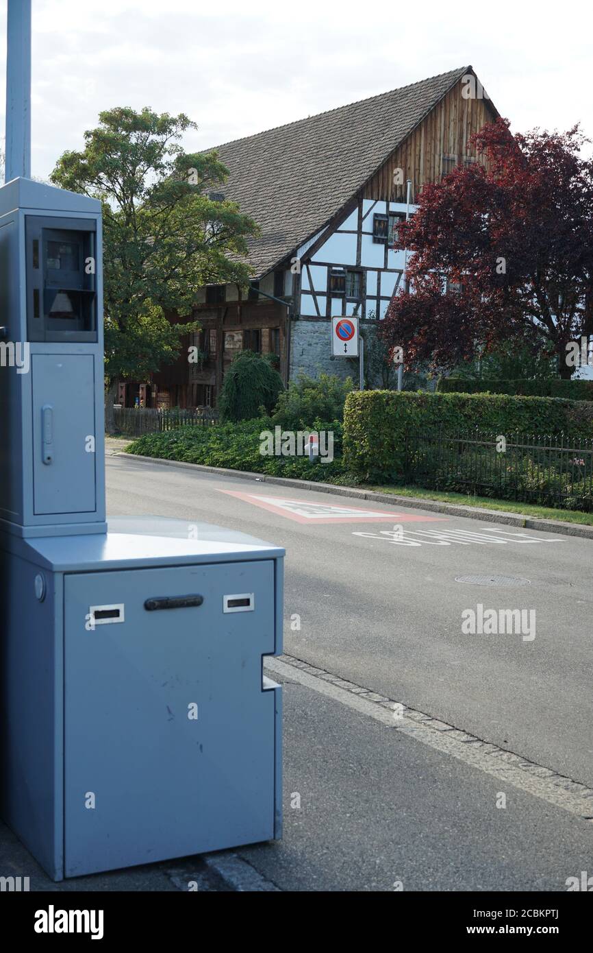 Radar photo de sécurité en Suisse, route près d'une maison blanche avec clôture de haie verte et feu de rue avec signalisation routière. Banque D'Images