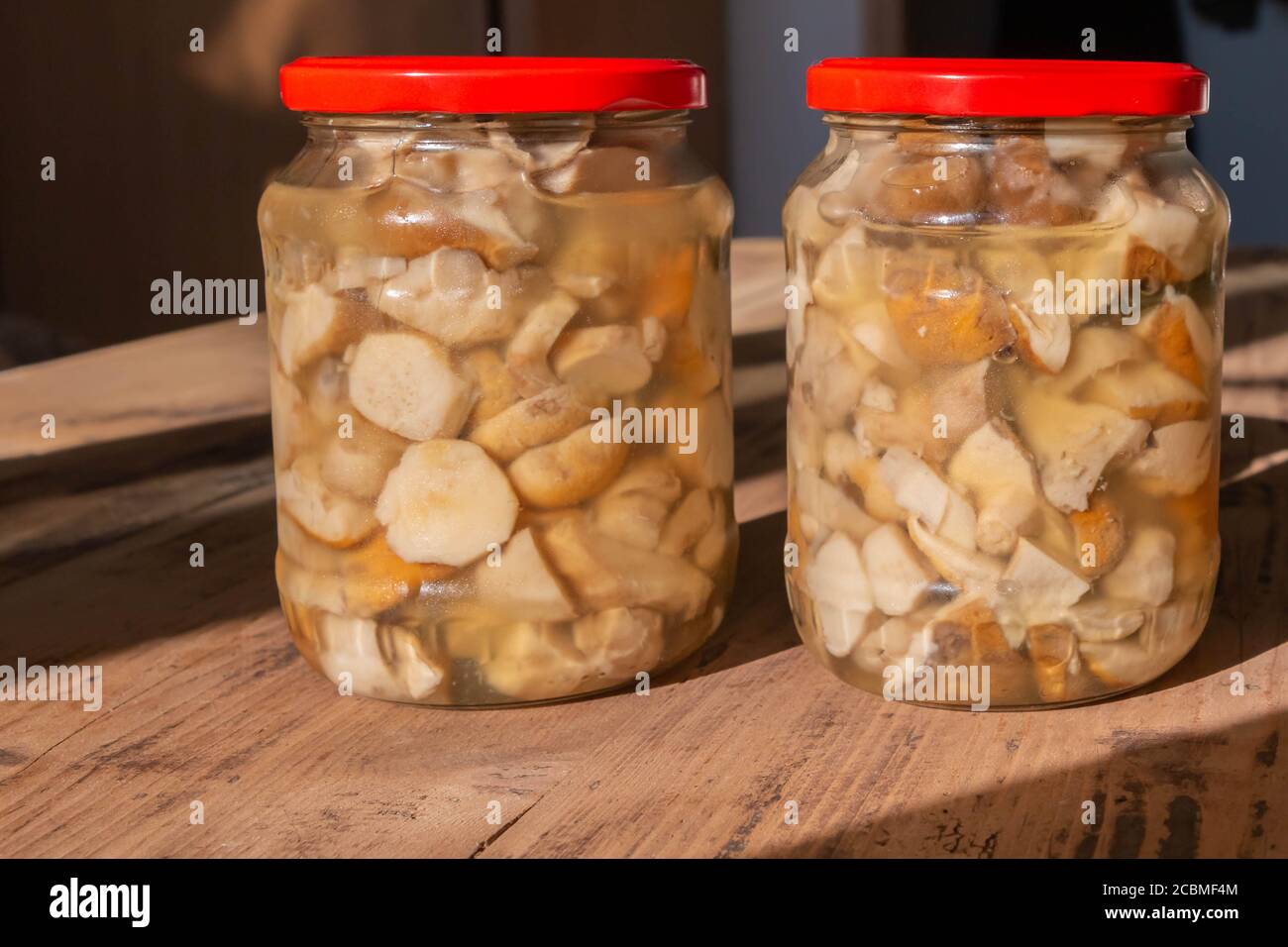 Champignons comestibles en conserve boletus en pots de verre sur fond de bois. Champignons préparés en verre sur une table en bois rustique au soleil. Presse maison Banque D'Images