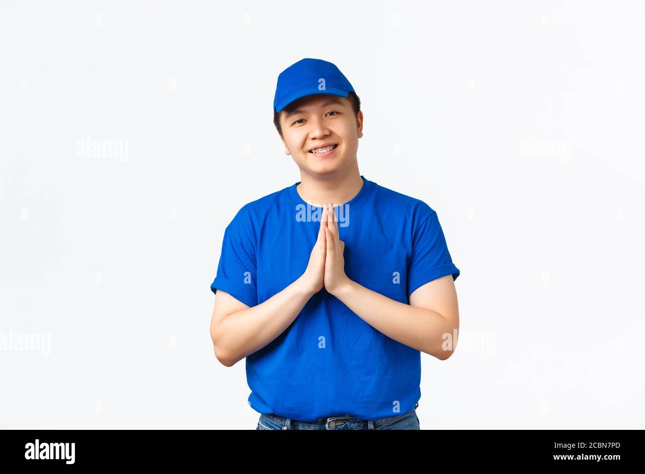 Beau liveur asiatique sympathique, uniforme bleu, tenant les mains dans les plis, paumes ensemble pour remercier, chérissez et valorisez les clients Banque D'Images