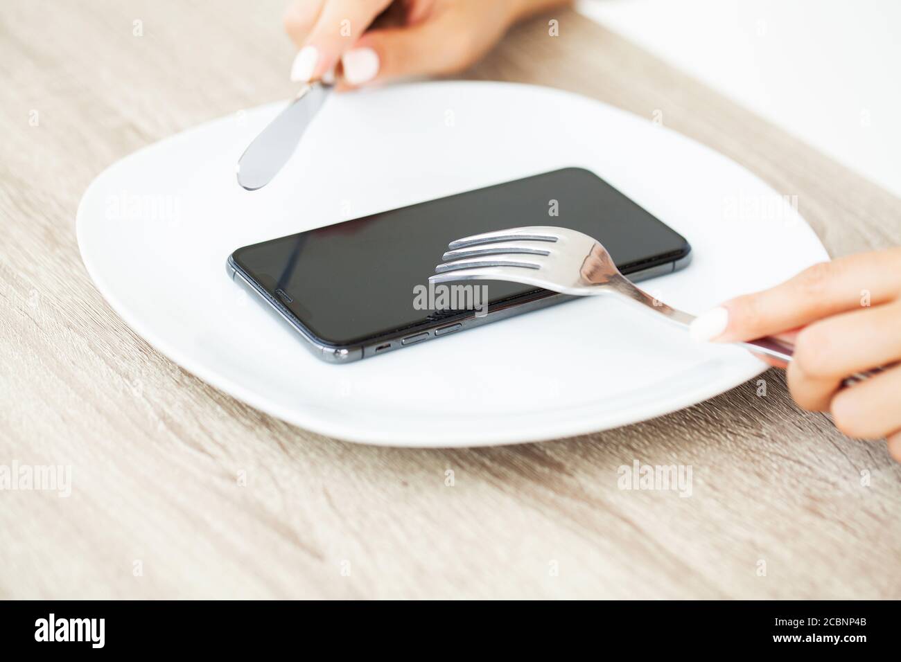 Dépendance au téléphone, gros plan les mains d'une femme tenant une fourchette et un couteau au-dessus du téléphone sur la plaque Banque D'Images