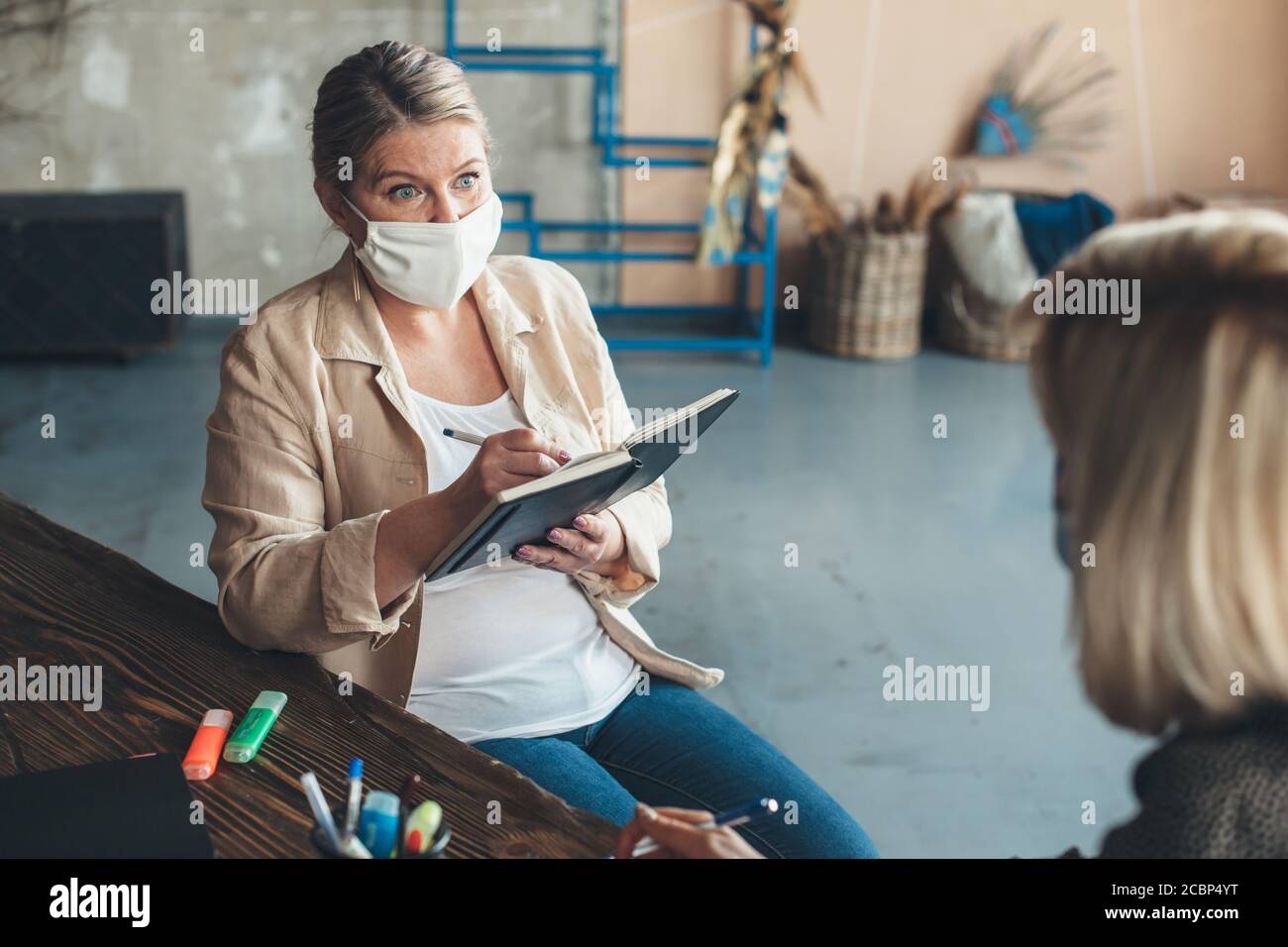 La femme caucasienne âgée portant un masque médical a un réunion avec un client à la maison écrivant quelque chose dans le ordinateur portable Banque D'Images