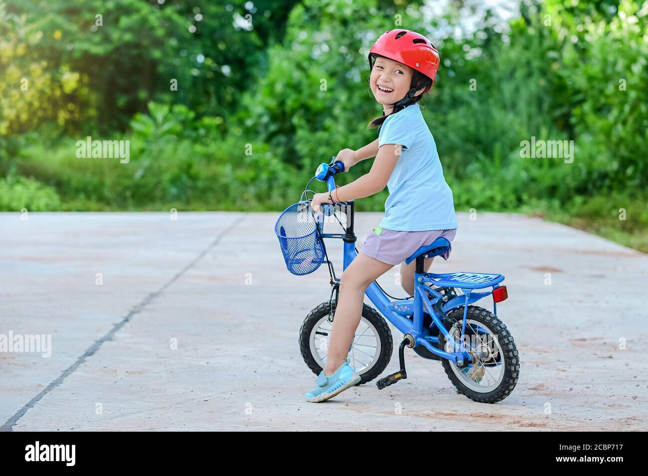 Bonne fille de vélo dans le parc dans le village pour la soirée avec l'exercice de lumière de coucher de soleil. Enfant actif portant un casque de vélo. Sécurité sports loisirs Banque D'Images