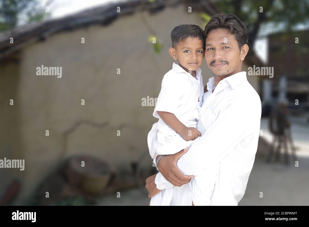 Portarait du jeune père indien rural et petit fils mignon dans des tissus traditionnels blancs avec fond de village, copier l'espace pour écrire du texte. Banque D'Images