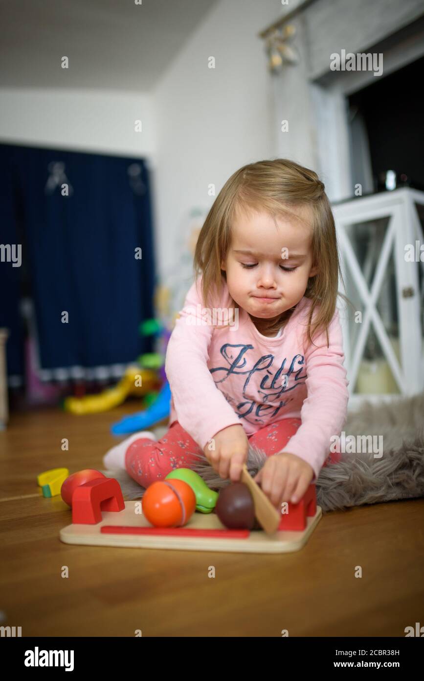 bébé fille de 2 ans à la maison coupant des fruits en peluche avec un  couteau en bois Photo Stock - Alamy