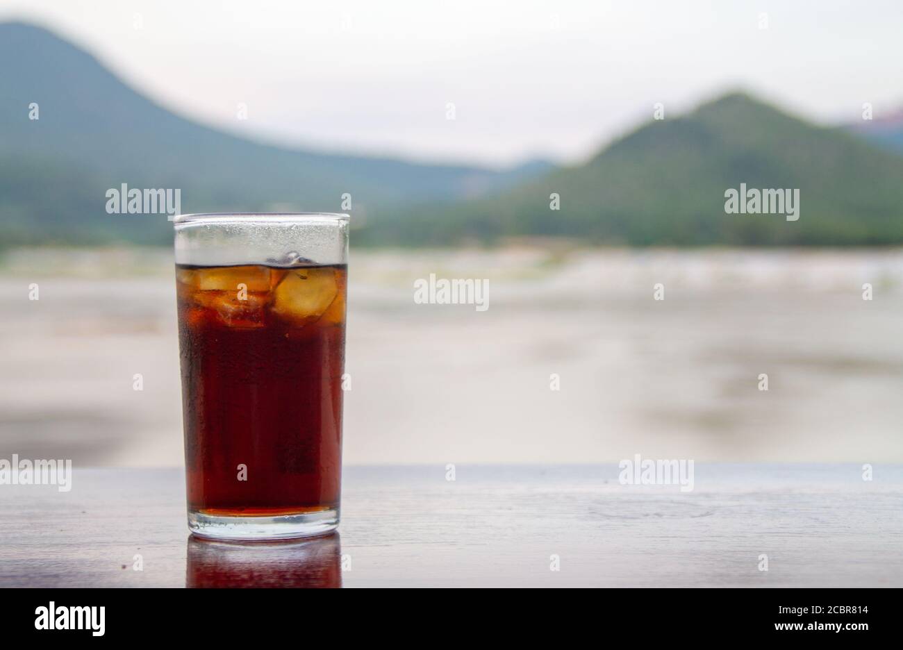 Cola en verre sur table avec fond de montagne et de rivière Banque D'Images