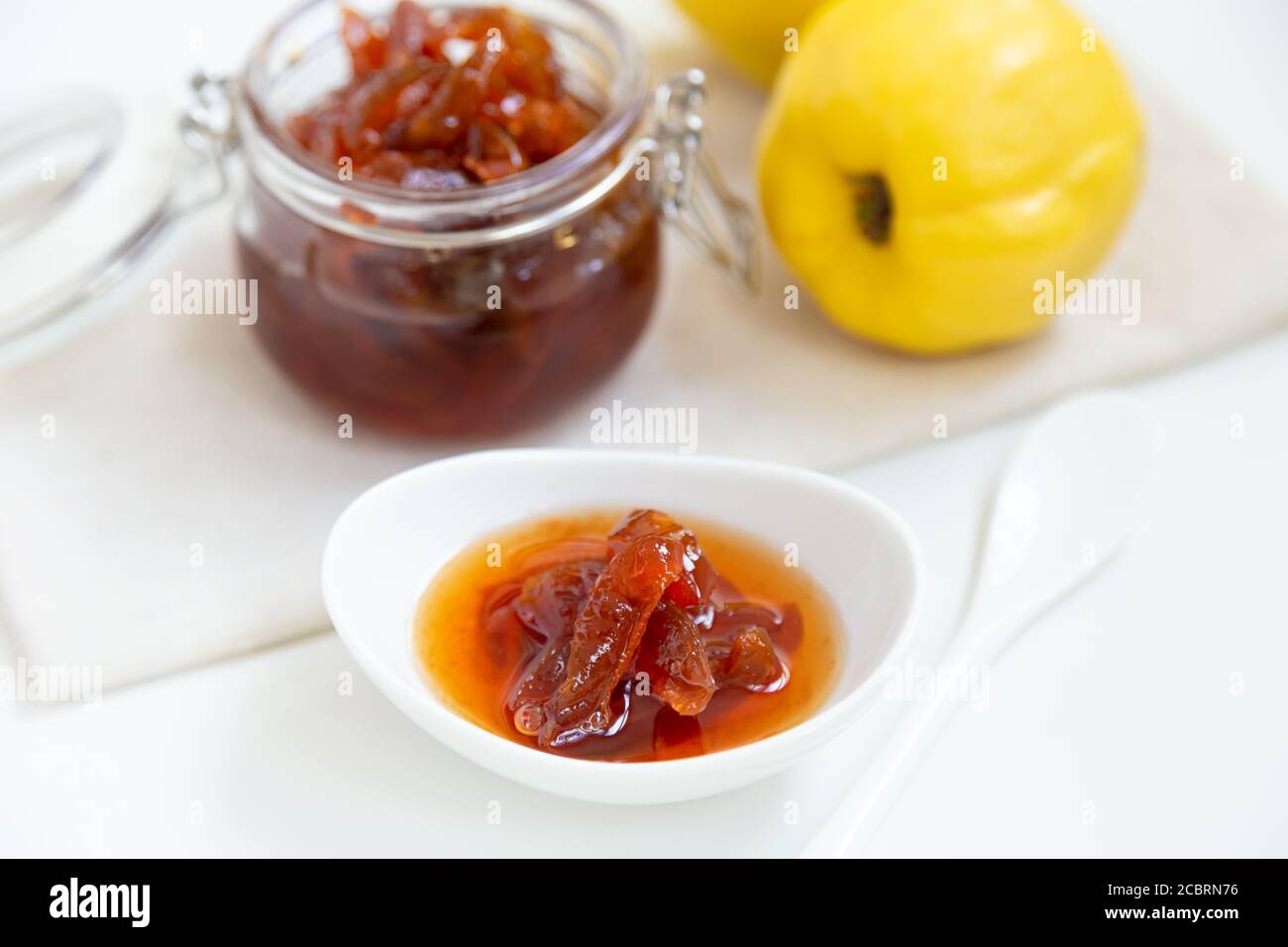 Confiture de coings maison dans un bol en porcelaine avec une tasse de thé. En arrière-plan se trouve un pot en verre avec confiture et coing. Banque D'Images