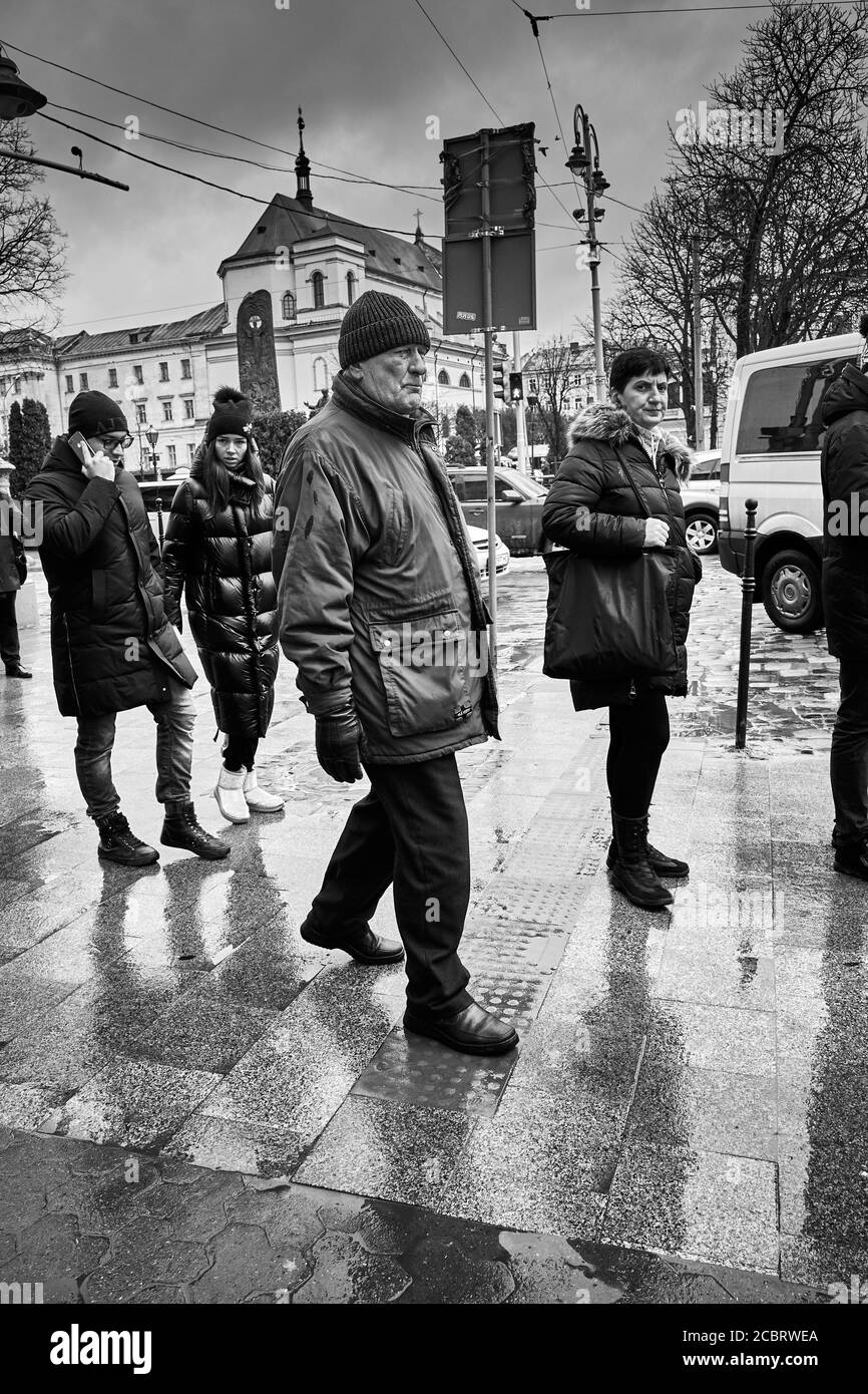 Habitants de la ville. Lviv/Ukraine - 30 janvier 2020 : des étrangers marchent sur le trottoir humide de la perspective Svobody regardant dans la caméra. Banque D'Images