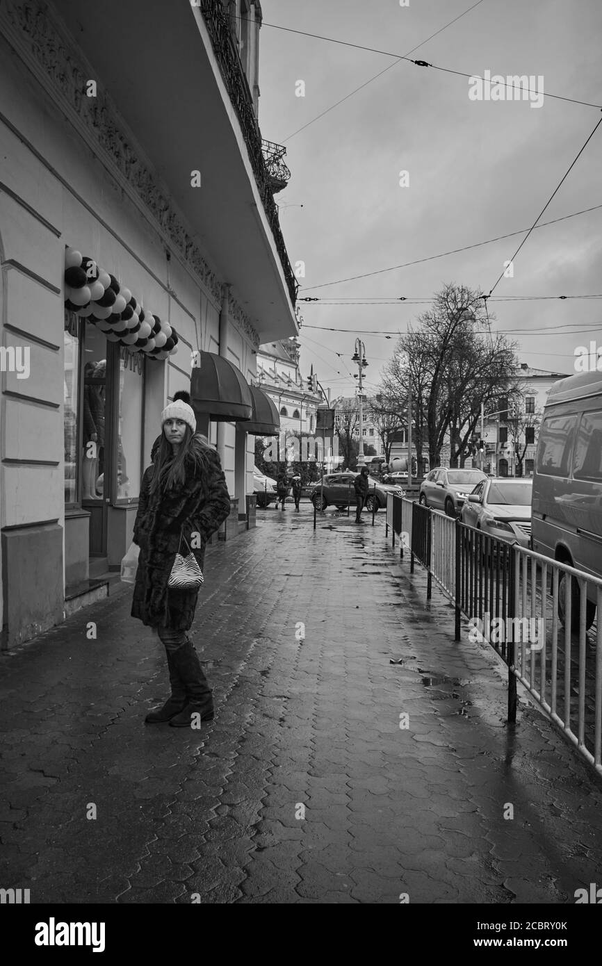Fille dans un manteau de fourrure. Lviv/Ukraine - le 30 janvier 2020 : une fille attend sur le trottoir humide de la rue Petra Doroshenka, à la froide journée d'hiver Banque D'Images