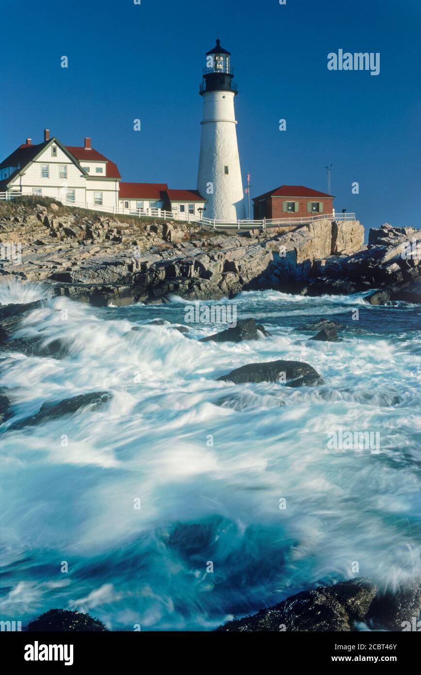 Portland Head Lighthouse dans le Maine au lever du soleil avec des vagues s'écraser sur un rivage rocailleux ci-dessous Banque D'Images
