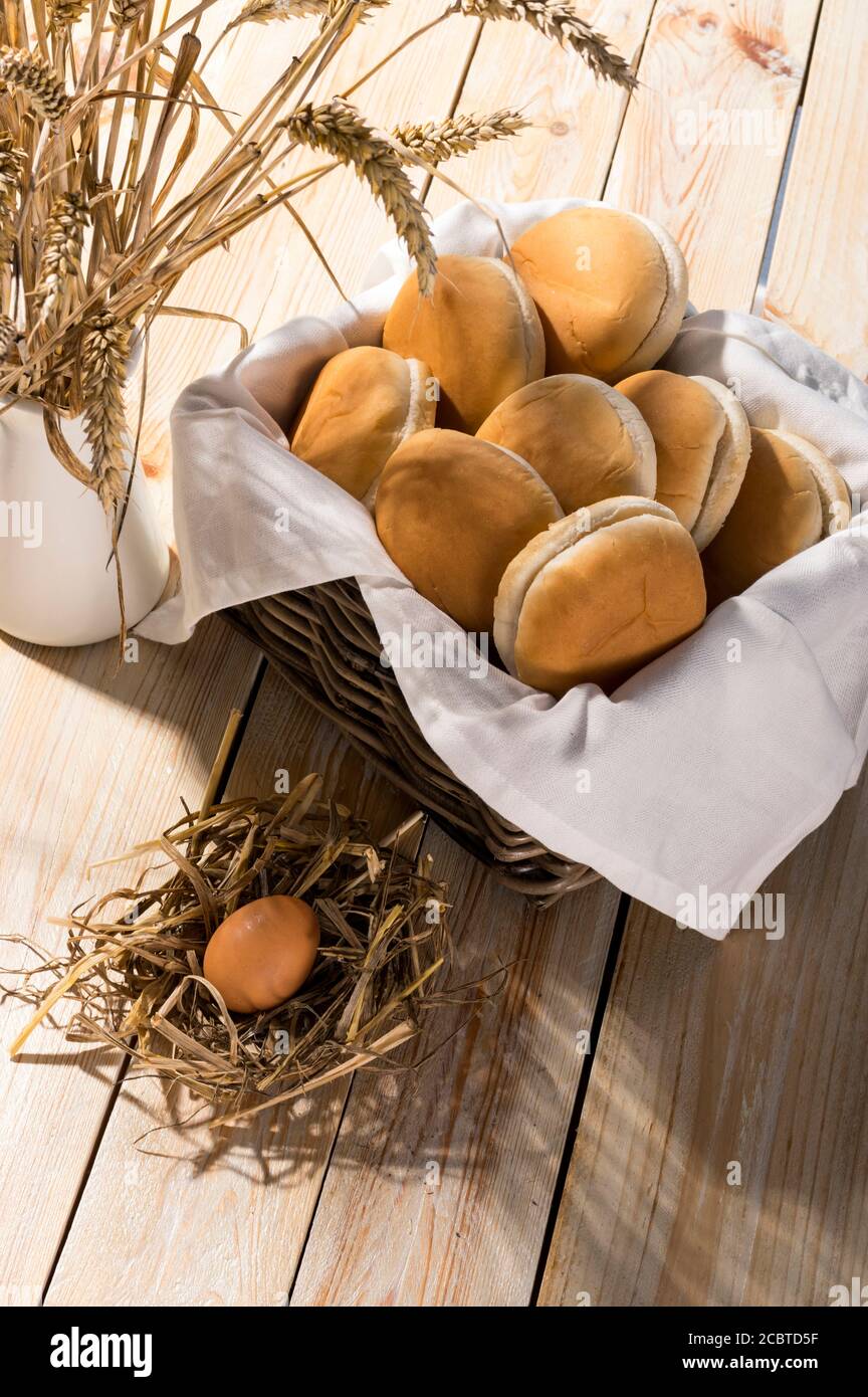 Petits pains de brioche frais et doux dans un panier sur fond de bois. Lumière vive pour des récoltes estivales ensoleillées. Banque D'Images