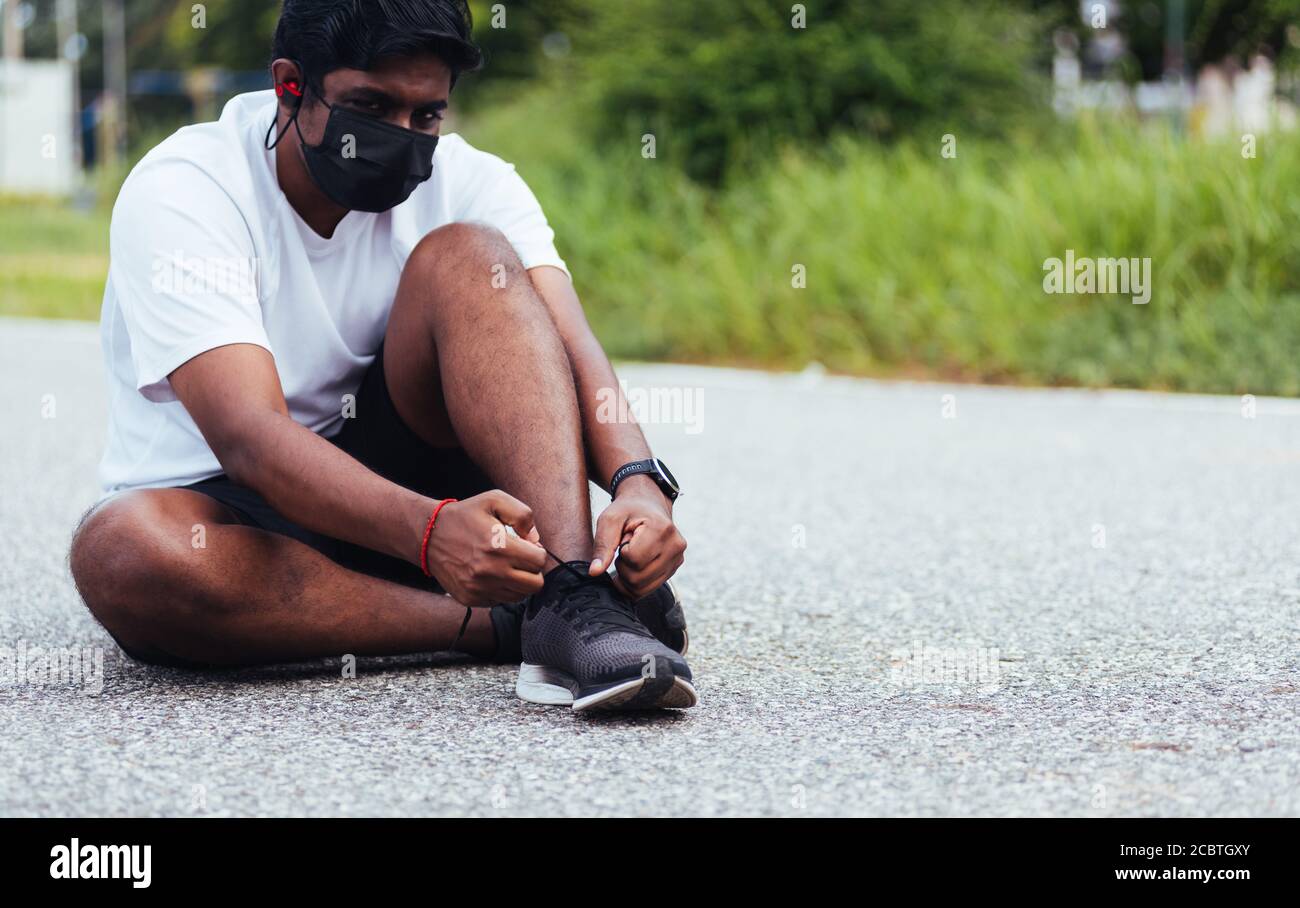 Gros plan asiatique sport coureur noir homme porter masque protection il a  cordonnet essayer des chaussures de course à pied se préparer pour le  jogging et courez au niveau du terrain extérieur