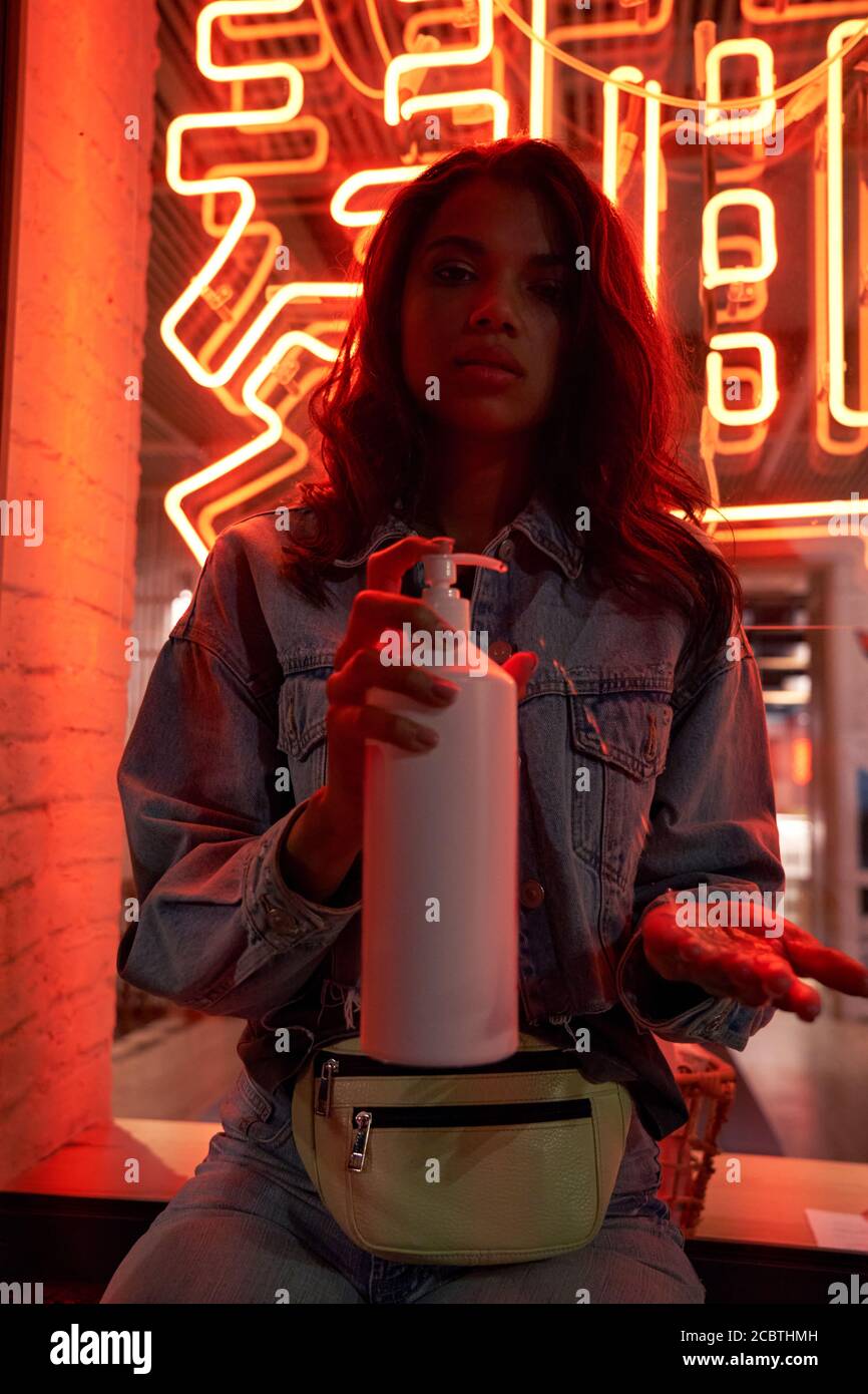 Hipster cool African gen z girl en utilisant l'assainisseur sous le néon rouge signe nuit lumière. Banque D'Images
