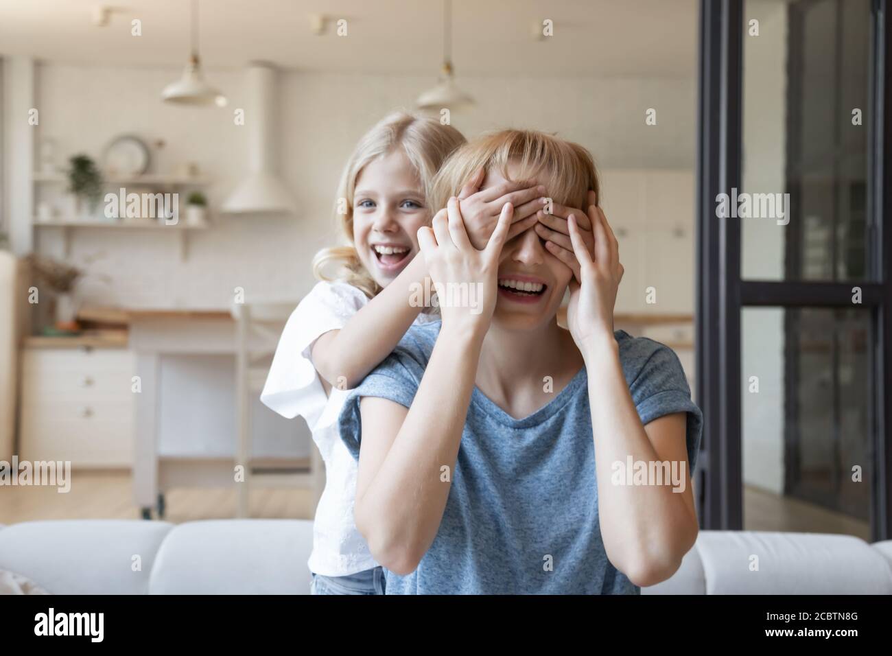 Petite fille naughty fermer les yeux de la mère riant avec des paumes Banque D'Images