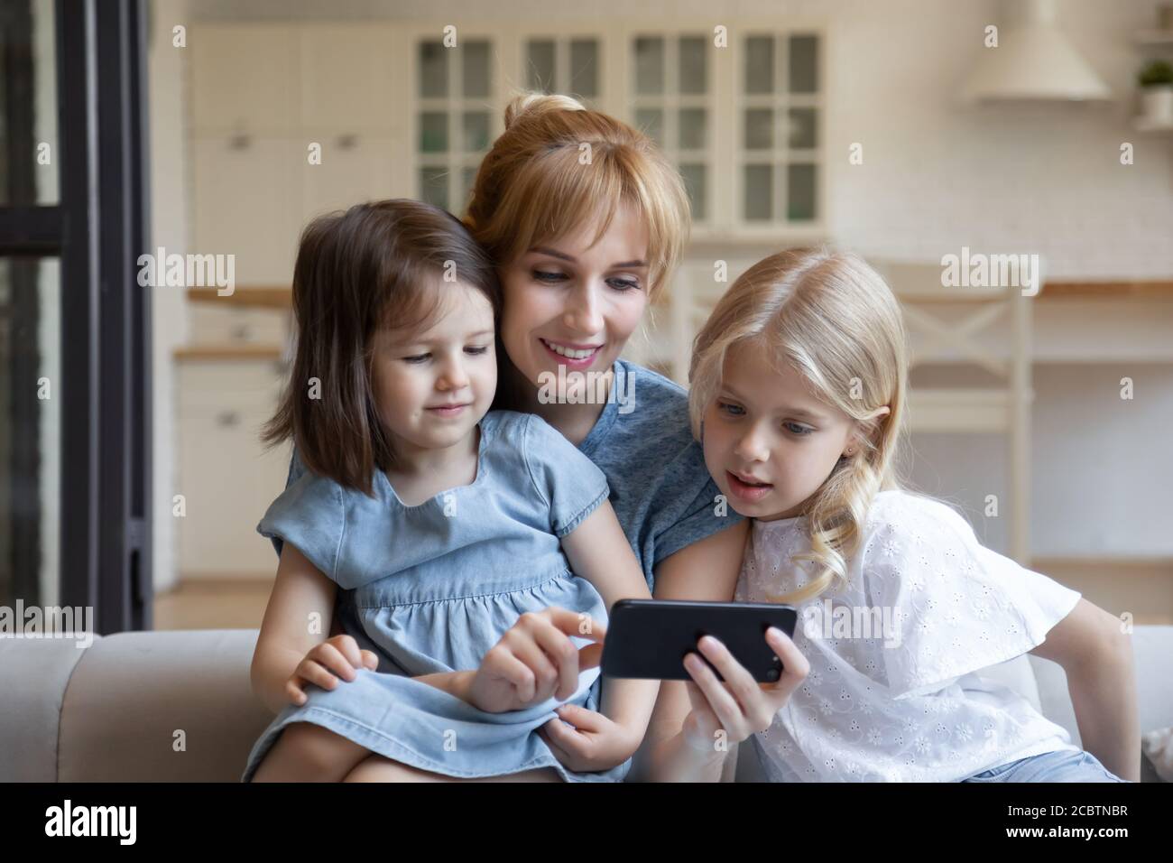 Une mère heureuse passe du temps libre avec ses filles en utilisant son smartphone ensemble Banque D'Images
