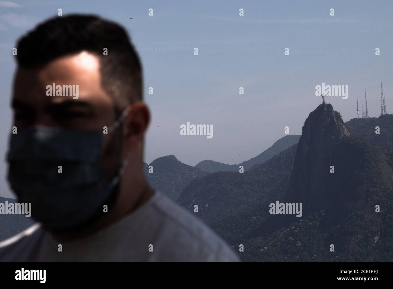 Rio de Janeiro, Brésil. 15 août 2020. Un homme avec un garde-bouche se dresse sur le sommet de la montagne Sugarloaf avec la statue du Christ en arrière-plan. Après des mois de fermeture en raison de la pandémie de Corona, le téléphérique menant au mont Sugarloaf a rouvert. Le Brésil est actuellement le deuxième pays le plus touché au monde par le virus corona. Crédit : Ian Cheibub/dpa/Alay Live News Banque D'Images