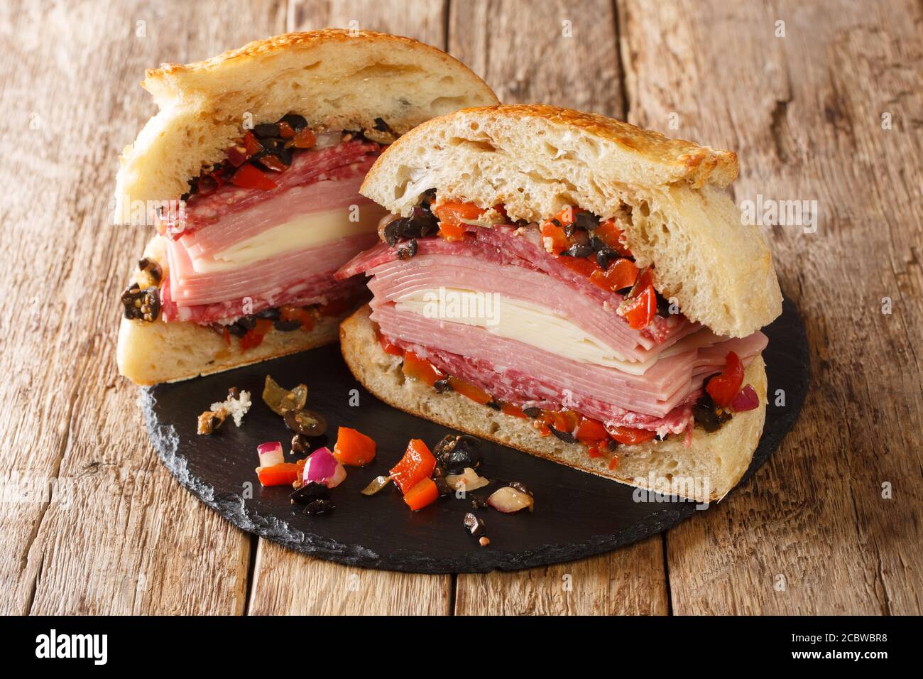 Sandwich Muffuletta de la Nouvelle-Orléans un monstre d'un sandwich rempli haut avec plusieurs types de viande et de fromage, et une salade d'olive perky gros plan sur une ardoise Banque D'Images