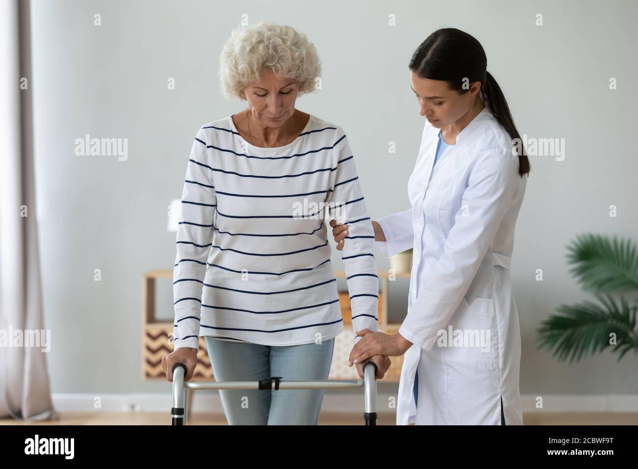 Travailleur médical aidant une femme handicapée mûre à marcher avec le cadre. Banque D'Images