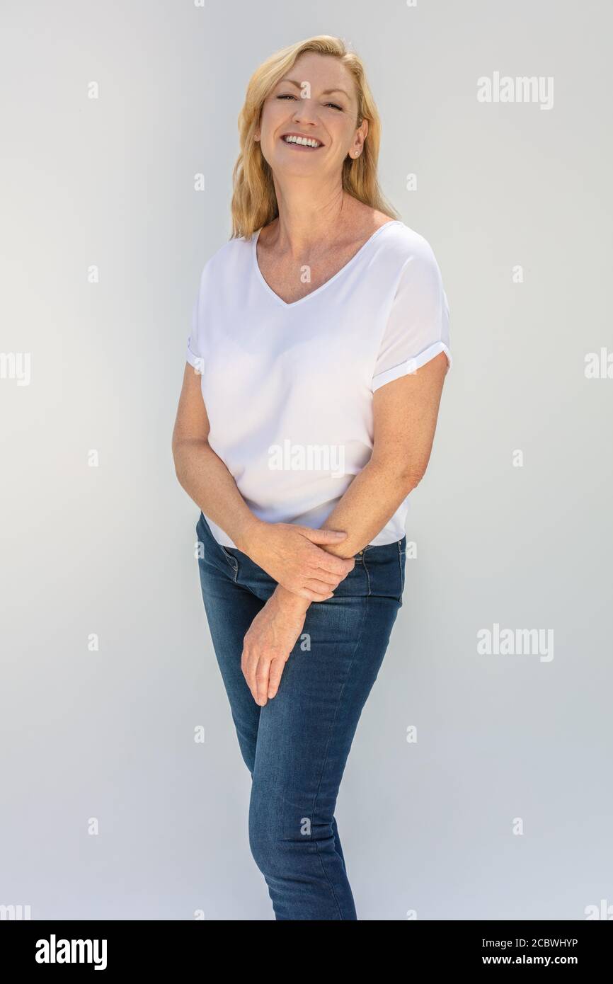 Portrait studio d'une jolie femme blonde d'âge moyen souriante sur un fond blanc portant un t-shirt blanc et bleu jeans Banque D'Images