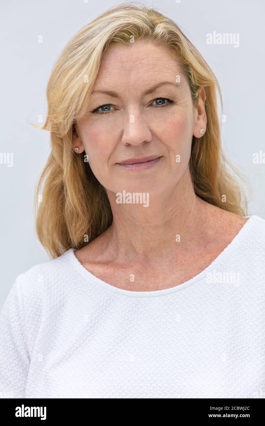 Portrait studio d'une jolie femme blonde d'âge moyen souriante sur fond blanc Banque D'Images