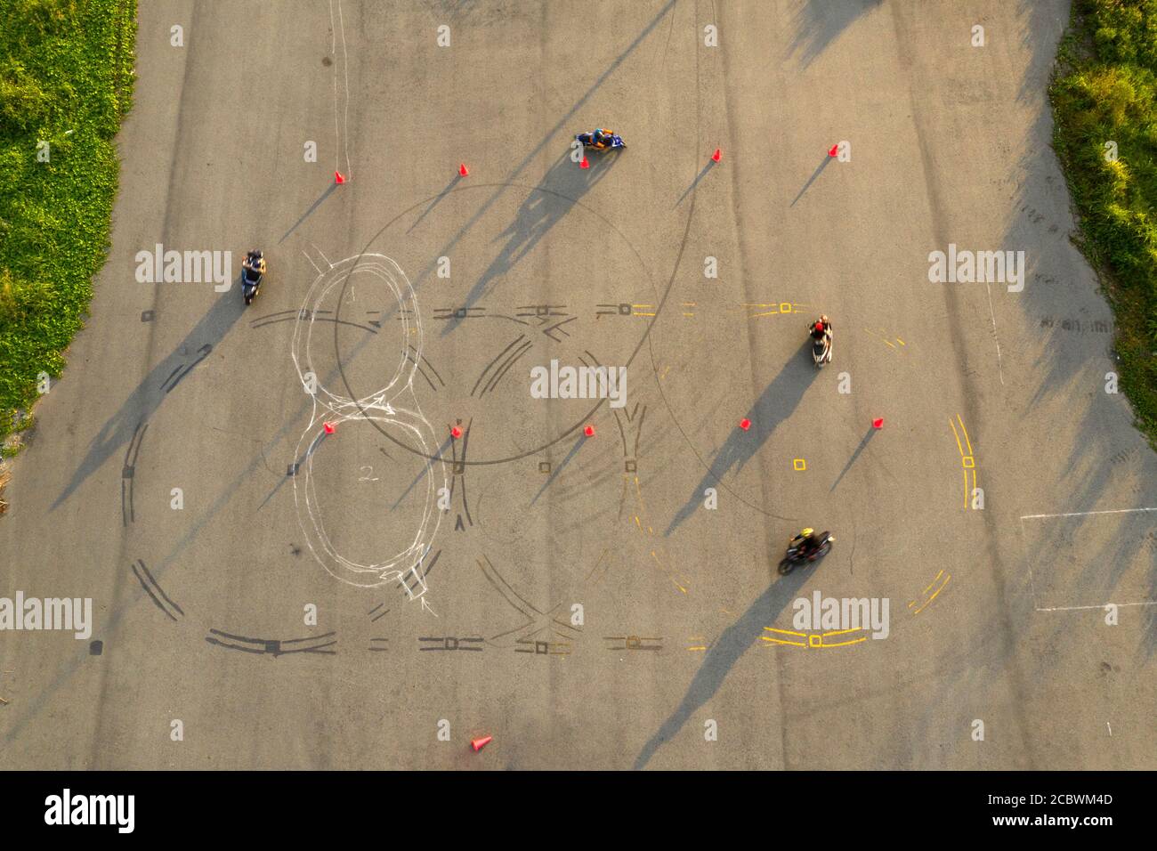 vue aérienne de haut en bas de quatre cavaliers s'amusant sur un parcours avancé de formation de moto slalom entre des cônes orange avec de longues ombres, peintes Banque D'Images
