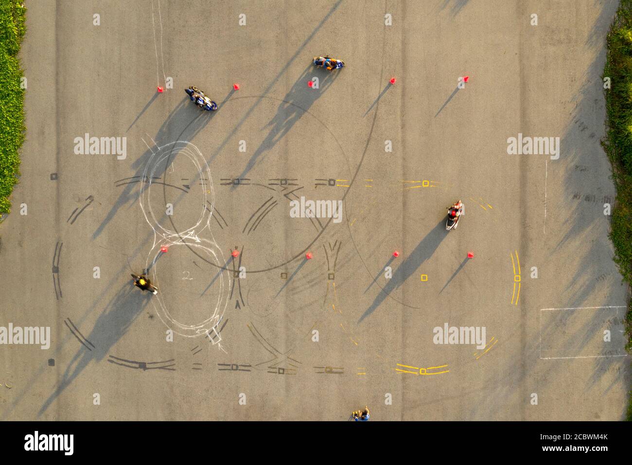 vue aérienne de haut en bas de quatre cavaliers s'amusant sur un parcours avancé de formation de moto slalom entre des cônes orange avec de longues ombres, peintes Banque D'Images