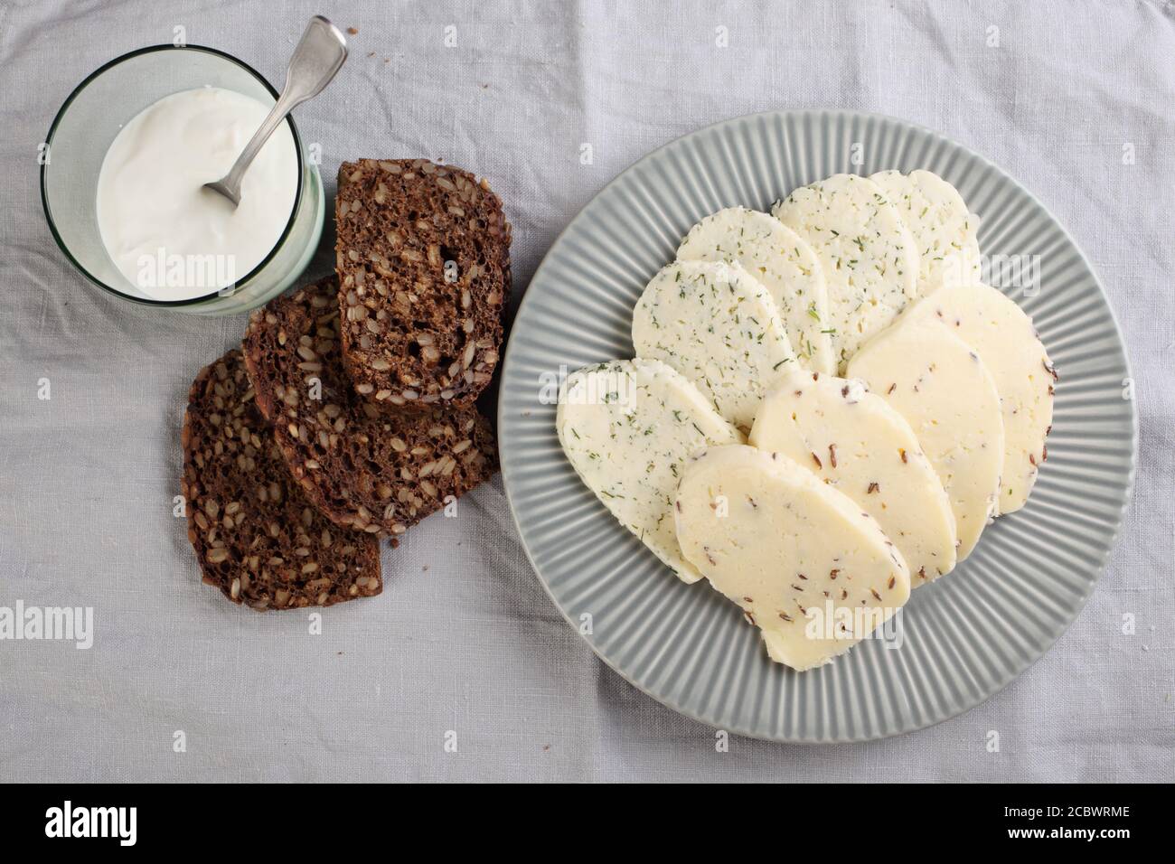 Fromages estoniens au cumin, à l'aneth et à l'ail, tranchés de pain de seigle aux grains, et une tasse de crème aigre Banque D'Images