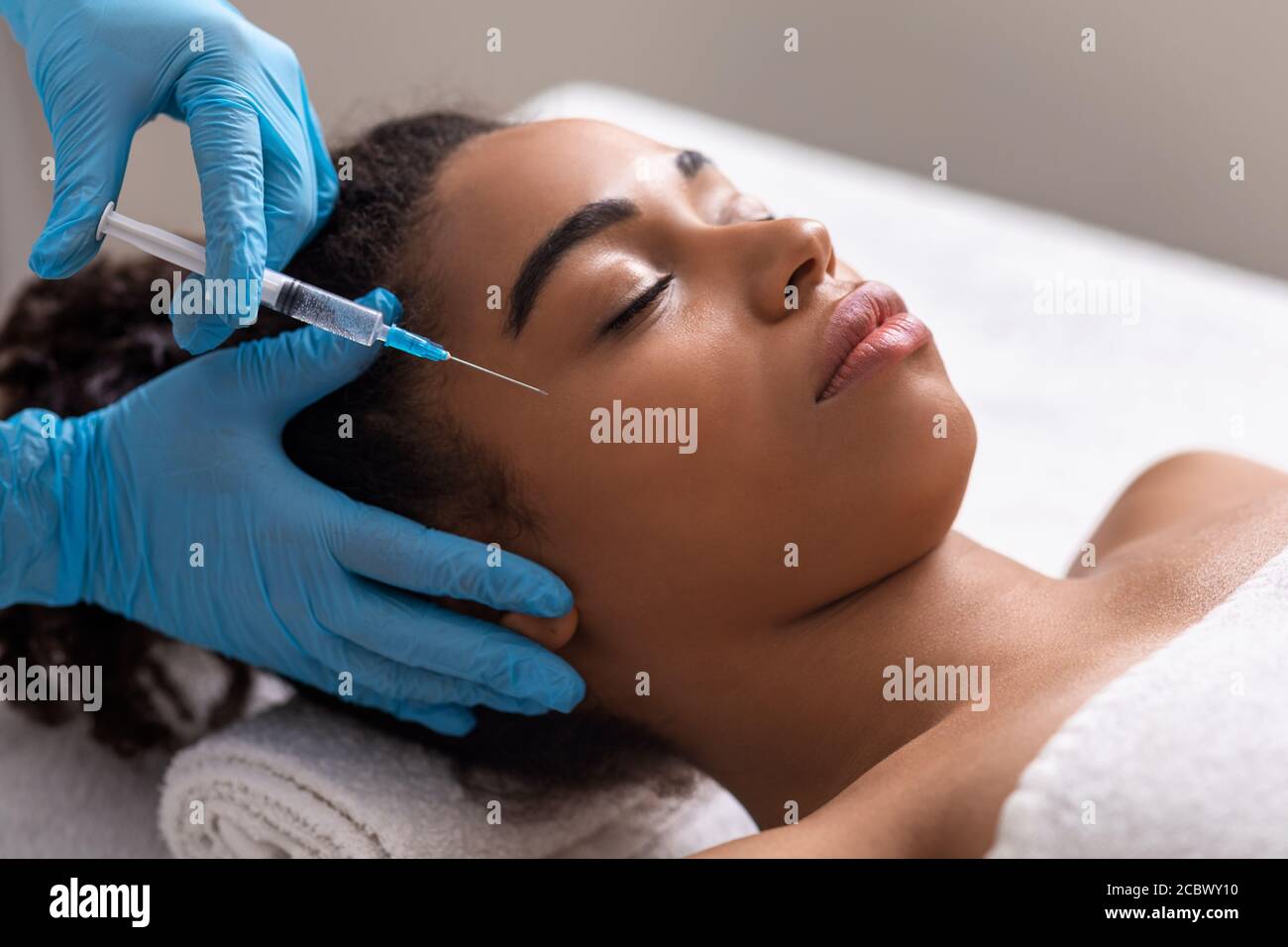 Jeune femme noire recevant une injection de zone oculaire au salon de beauté Banque D'Images Jeune femme noire recevant une injection de zone oculaire au salon de beauté Banque D'Images