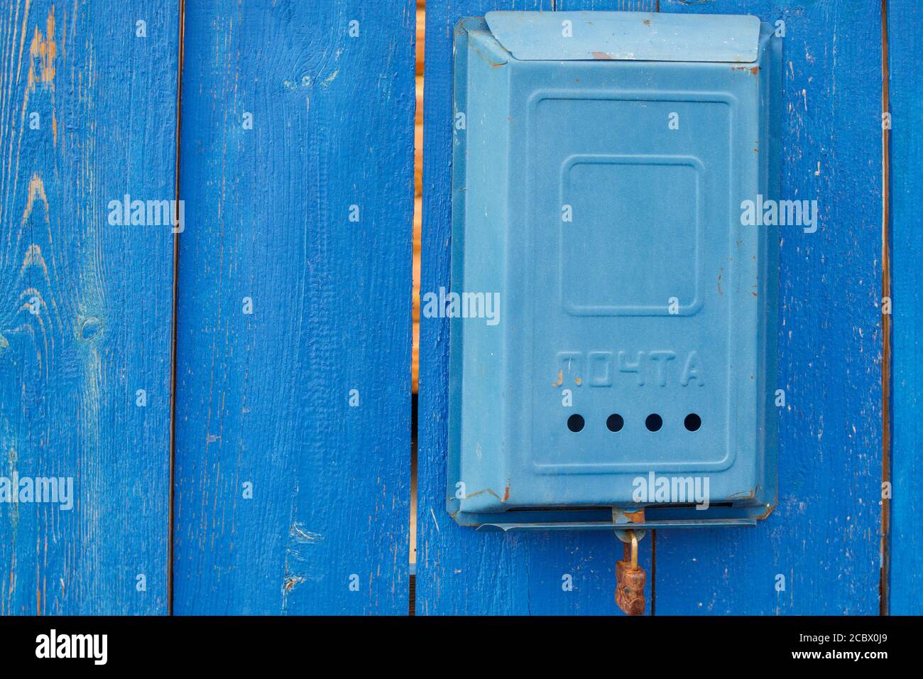 Une ancienne boîte aux lettres soviétique bleue avec l'inscription Mail et une serrure rouillée accrochée à une clôture en bois bleu rural. Banque D'Images