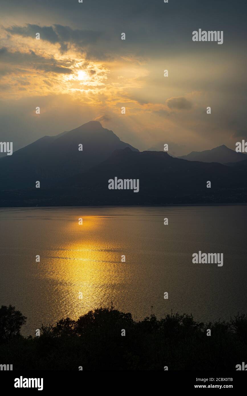 Le soleil du soir brille à travers les nuages orageux au-dessus de Monte Pizzocolo et du lac de Garde, en Italie Banque D'Images
