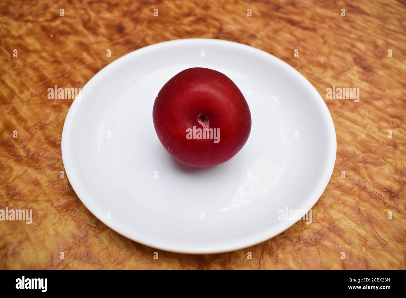 Prune unique isolée sur fond blanc. Gros plan d'un fruit. Prune cerise rouge bordeaux violet Banque D'Images