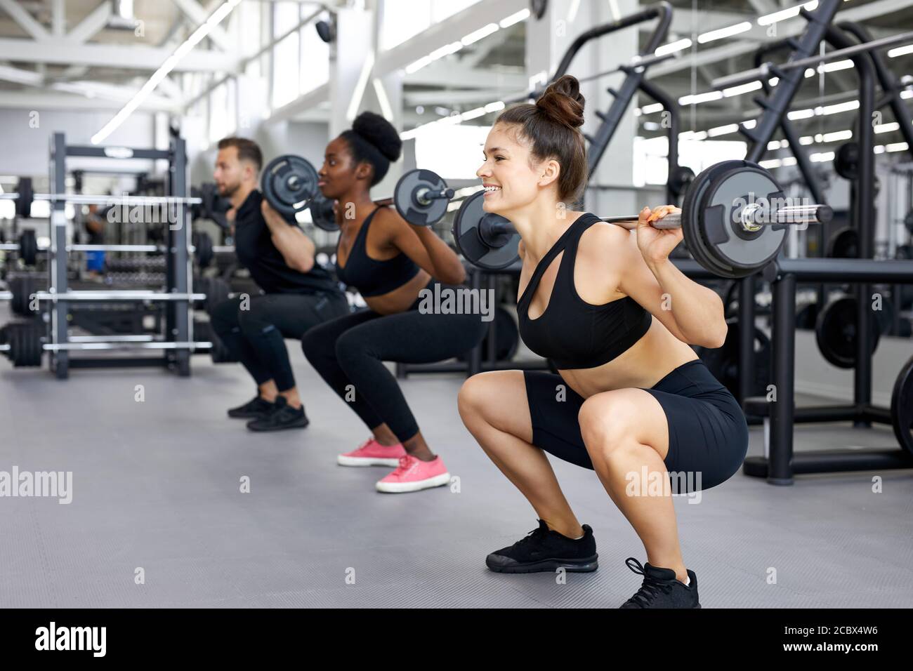 les sportifs, groupe multiethnique, font des exercices avec poids lourds en salle de gym. jeune homme et femme divers entraînement, ont le corps musculaire Banque D'Images