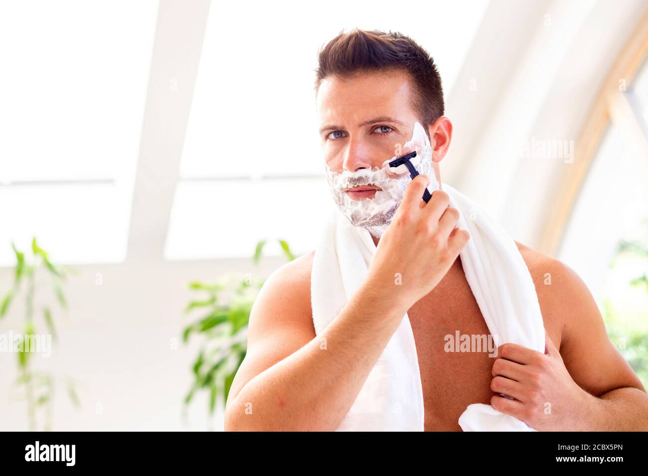 Prise de vue d'un beau homme avec une serviette autour de son cou en  utilisant de la mousse à raser tout en se secouant devant le miroir de la  salle de bains