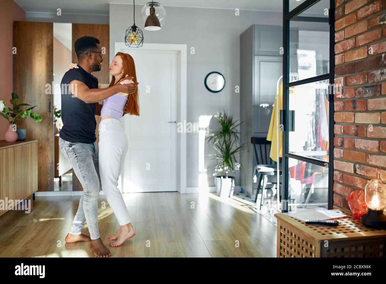 vue latérale sur une belle femme dansant avec un petit ami à la maison. couple interracial en tenue décontractée en mouvement. deux coeurs remplis d'amour. Banque D'Images