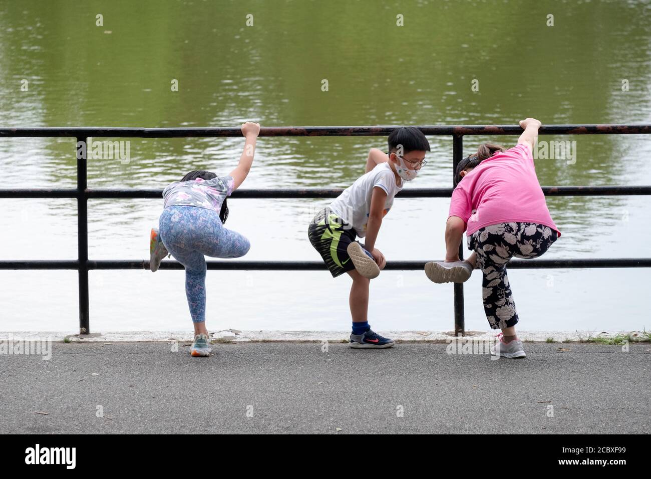Une mère asiatique américaine et ses enfants s'étirent ensemble au bord du lac dans le parc de Kissena avant une promenade d'exercice tôt le matin. À Flushing, Queens, N. Banque D'Images