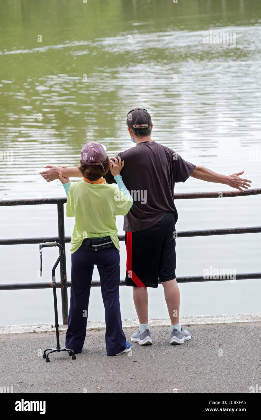 Un aide aide aide un homme ayant des problèmes de santé à faire sa routine d'étirement. Dans un parc à Flushing, Queens, New York. Banque D'Images