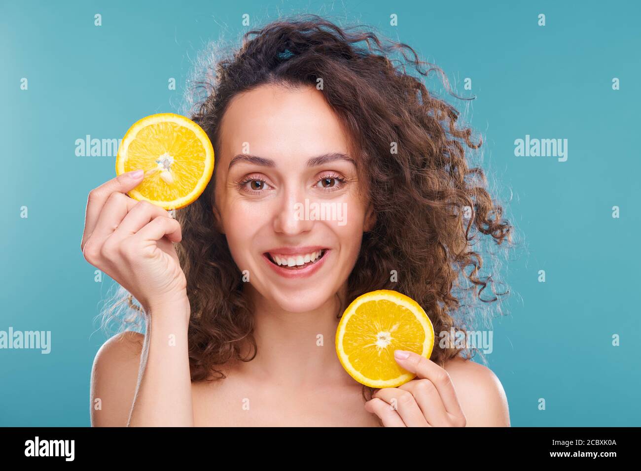 Joyeuse femelle avec de longs cheveux ondulés foncés tenant deux tranches d'orange juteuse fraîche Banque D'Images